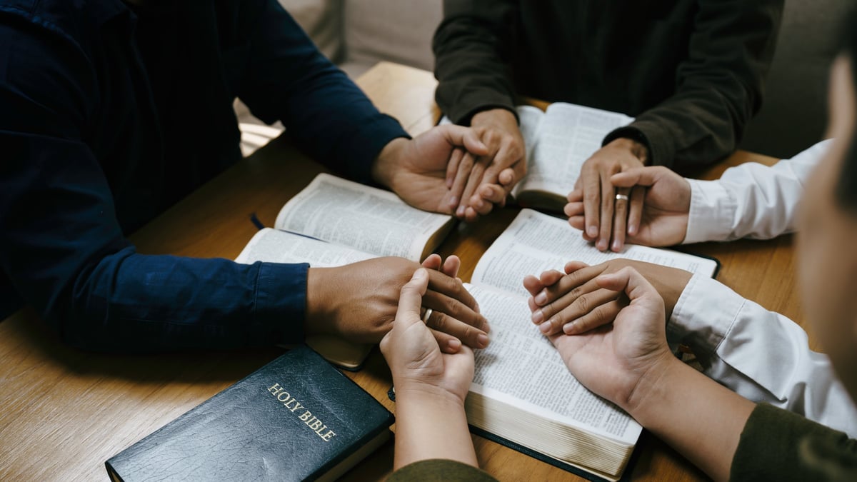 A diverse group holding hands in prayer around a Bible