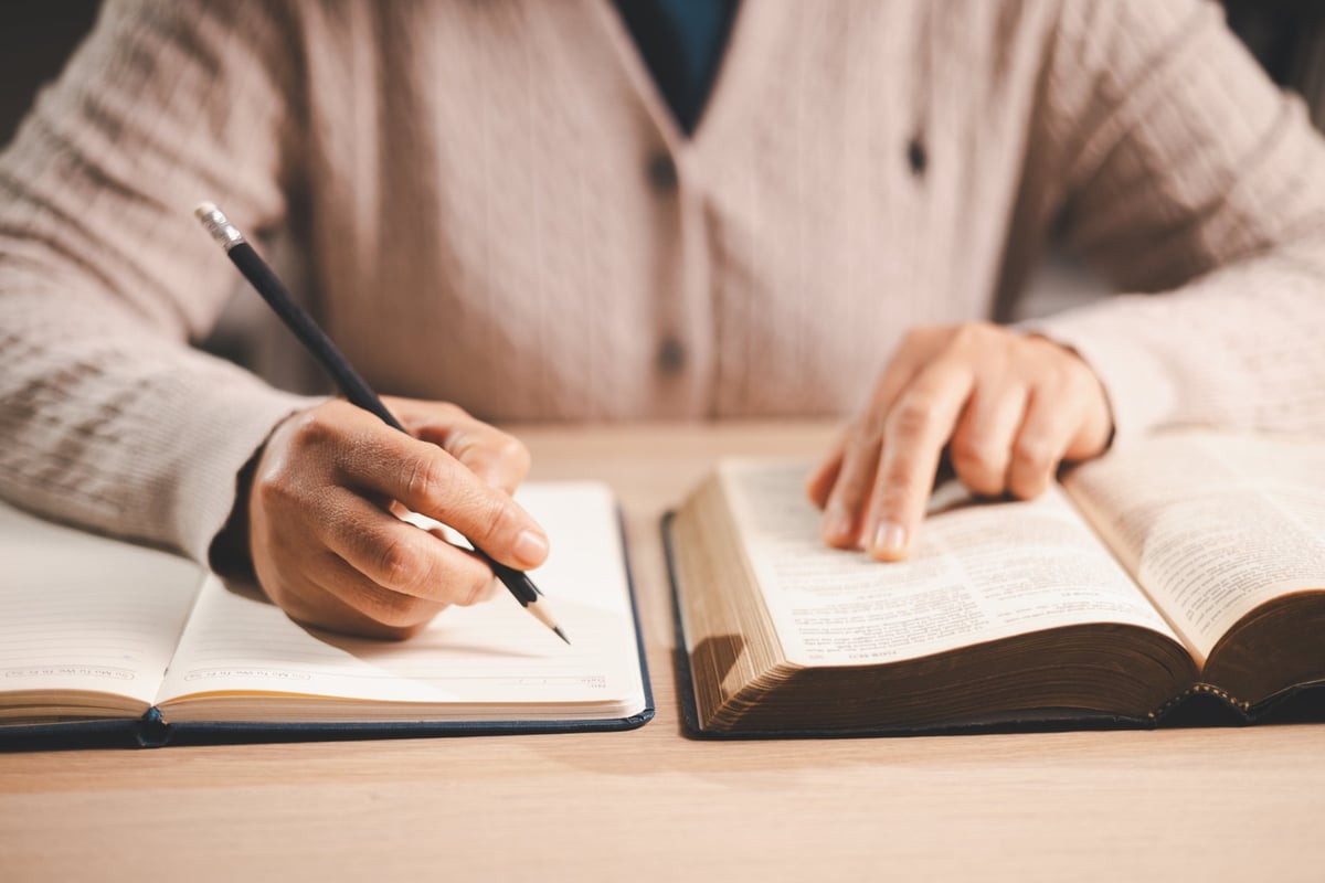 Hands taking notes while studying an open Bible