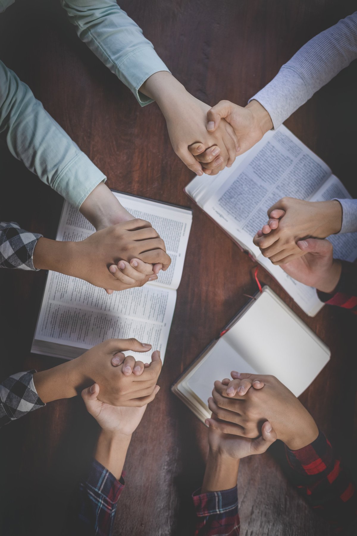 A diverse group holding hands in prayer around a Bible